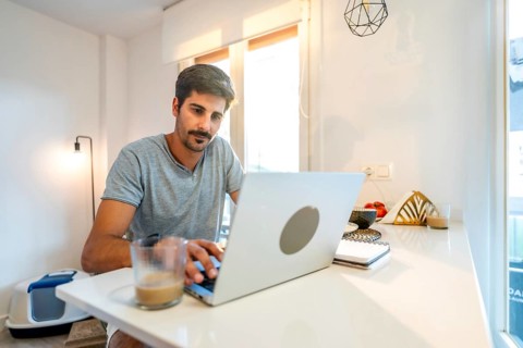 Young man concentrating on his laptop, enjoying a coffee while working remotely from his stylish