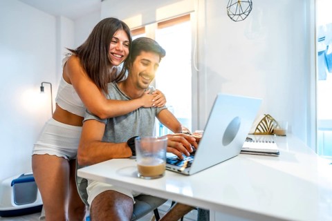 Young smiling couple using laptop at home, woman hugging man working on computer, modern bright