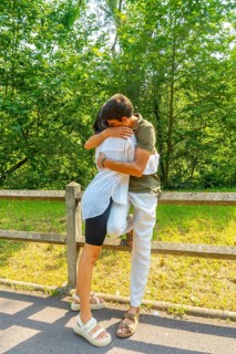 Romantic couple hugging near a wooden fence in a park, enjoying a sunny summer day surrounded by