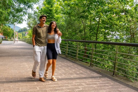 Young couple enjoying a leisurely stroll across a bridge in a green park, embracing the tranquility