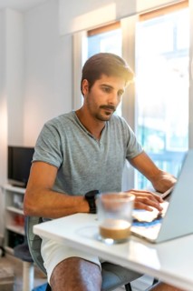 Young man concentrating on his laptop, working remotely from his bright home office while enjoying