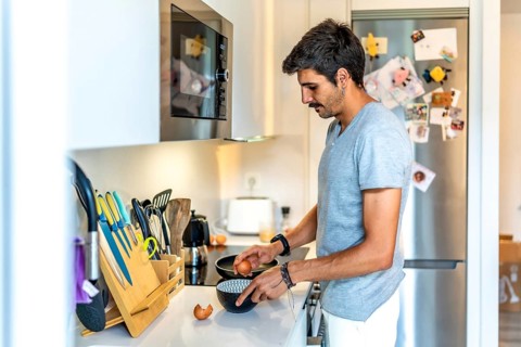 Young man cracking eggs into a bowl, preparing to cook breakfast or a meal in his modern, well