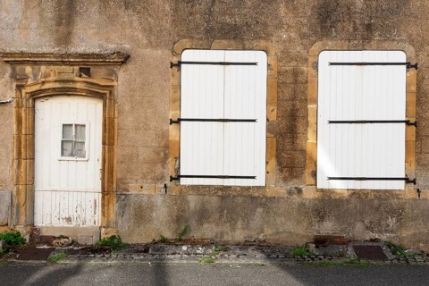 Door and 2 white, closed windows made of wood, historic house facade, yellow sandstone, Marville,