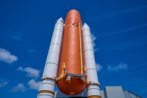 Large orange space shuttle with two launch vehicles against a blue sky, Kennedy Space Center