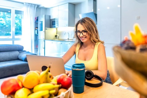 Young woman working remotely from her home office using laptop, enjoying healthy lifestyle with