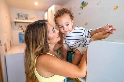 Smiling mother holding hands with her baby son while playing in a decorated children's bedroom
