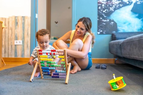 Happy mother watching her baby boy playing with a colorful abacus, developing early math skills in