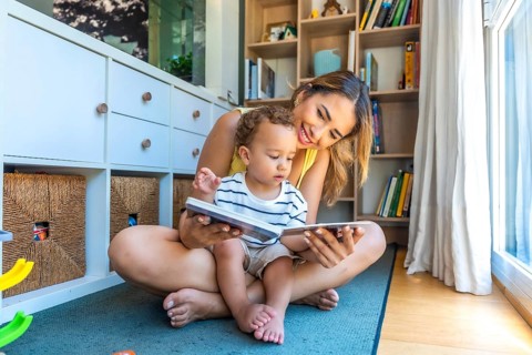 Smiling mother and baby son sharing joyful moments while reading books together, fostering a love