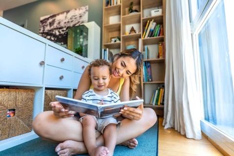 Happy mother and son enjoying quality time together, reading a book on the floor of their cozy