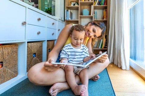 Young mother sitting on the floor reading a book with her little son, enjoying quality time