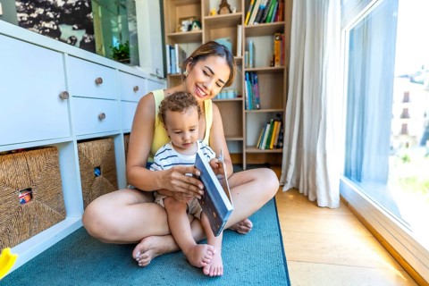 Happy mother and her little son reading a book together, sitting on the floor in the living room
