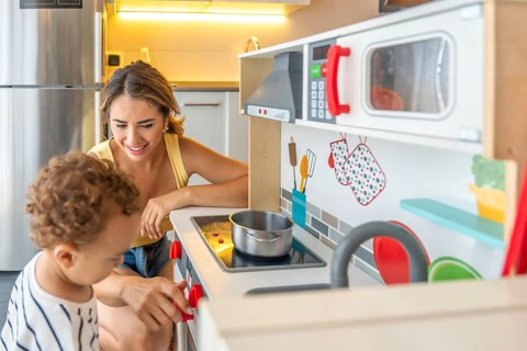 Mother and son having fun playing with toy kitchen at home, enjoying quality time together and