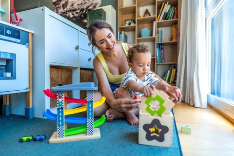 Happy mother and her cute son are playing together with colorful educational toys in a modern