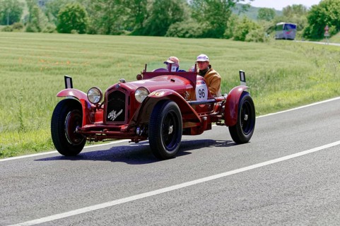 A red classic car drives on a country road through a green landscape, classic car, car race, Mille