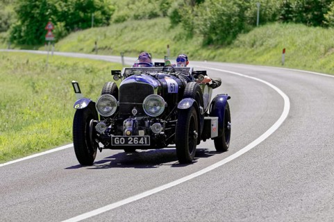 Dark blue classic car with two men on a country road in a green environment, classic car, car race,