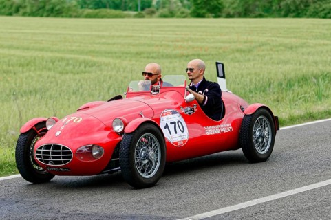 A classic red car with two people driving on a country road, classic car, car race, Mille Miglia,