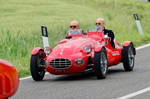 A red sports car with two drivers drives on a rural route, classic car, car race, Mille Miglia,