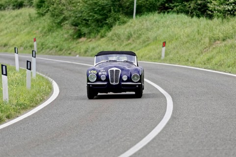 A dark classic car drives alone on a winding country road, classic car, car race, Mille Miglia,