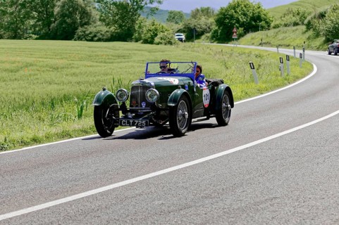 Green classic car drives on a winding country road through a green landscape, classic car, car