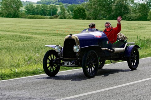 Black vintage car with two men, one waving, on road landscape in spring, vintage car, car race,