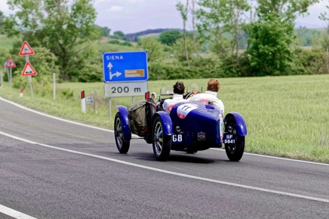 Blue classic car in the direction of Siena on a country road through the Italian countryside,