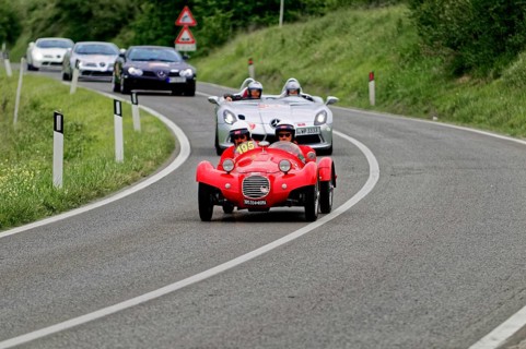 Two people with helmets in a red classic car on a country road, sporty-classic scene, classic car,