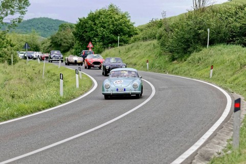 Blue vintage car leads a group of classic cars on a winding country road, picturesque surroundings,