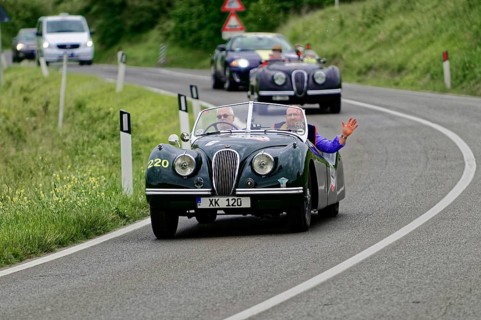 Two people in a green vintage convertible on a winding country road, casual atmosphere, vintage