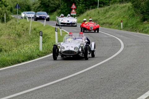 Silver racing car leads ahead of red classic car on winding country road, classic car, car race,