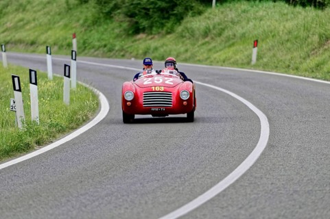 A red convertible sports car with two drivers on a winding country road, classic car, car racing,