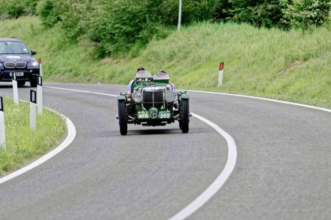 Green vintage car drives on winding country road, lined with green landscape, vintage car, car