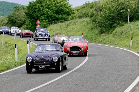 Black classic car followed by red and other classic cars on a winding road, dynamic race, classic