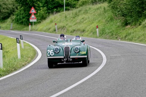 Two people in a green vintage convertible with racing numbers, fast drive on country road, vintage