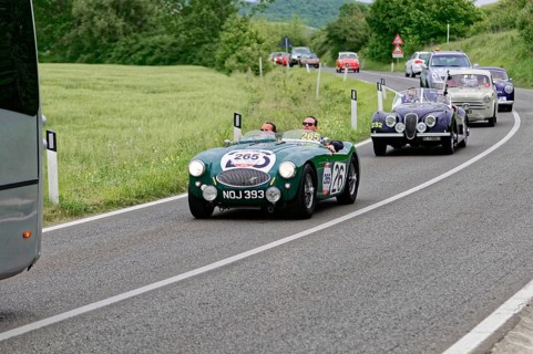 Green classic car in a row of vehicles on a winding country road, classic car, car race, Mille