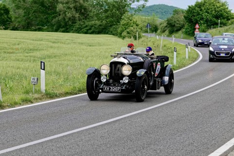 A classic vintage car with two drivers takes part in a car rally on a picturesque road, classic
