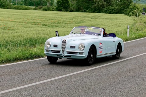 Blue convertible on a country road with green meadows in the background, classic car, car race,
