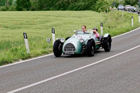 Grey classic car on a country road surrounded by green fields and trees, classic car, car race,
