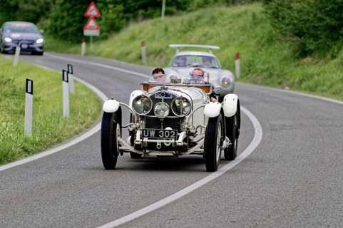 White classic car drives along a winding country road through a green landscape, classic car, car