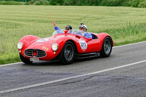 Two people joyfully driving a red Maserati on a country road, classic car, car race, Mille Miglia,
