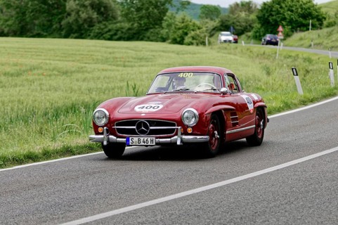A red Mercedes classic car drives along a picturesque country road surrounded by trees, classic