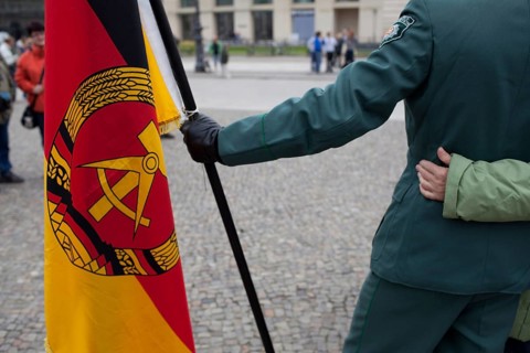 DEU Germany Berlin Actor with GDR flag is hugged by tourists while taking pictures. Scene on the