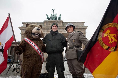 A riot police officer with the Berlin Bear and an actor in NVA uniform is photographed by a