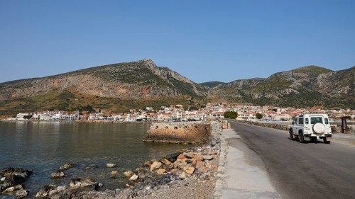 An off-road vehicle on a coastal road with a view of a city and mountains, Monemvasia, Monemvassia,