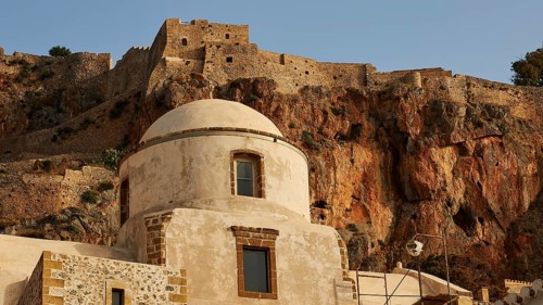 Soft morning light, historic buildings and fortress elements in front of an impressive rock wall,