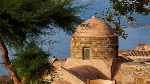 Soft morning light, view over a dome and the sea, framed by green trees and tiled roofs,