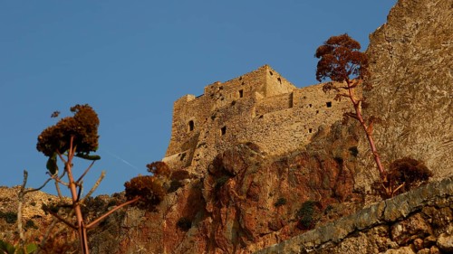 Soft morning light, old stone fortress on rocks with plants, under clear sky, Monemvasia,