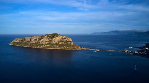 Drone shot, island in the sea, connected by bridge, mountains and sky in the background,