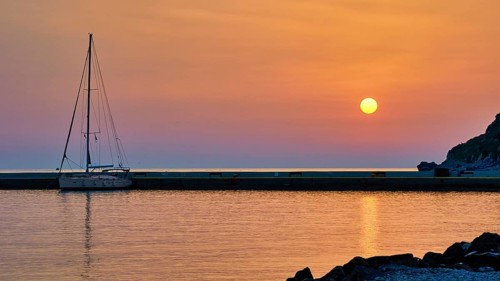 Sailing boat against orange sky and calm sea at sunrise, Monemvasia, Monemvassia, Malvasy,