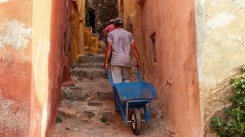 A man pulls a wheelbarrow up a narrow, colorful alley, Monemvassia, Malvasy, small Byzantine town,