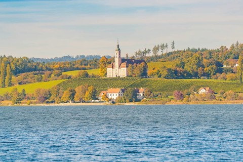 A church on a hill above autumn vineyards and a lake, surrounded by picturesque landscapes and